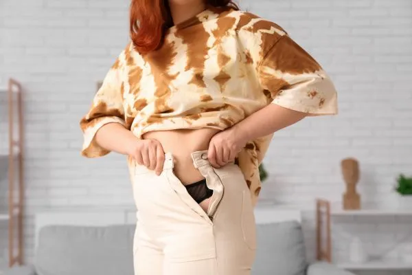 Image of woman trying to do her trousers up after pregnancy weight gain Buckingham